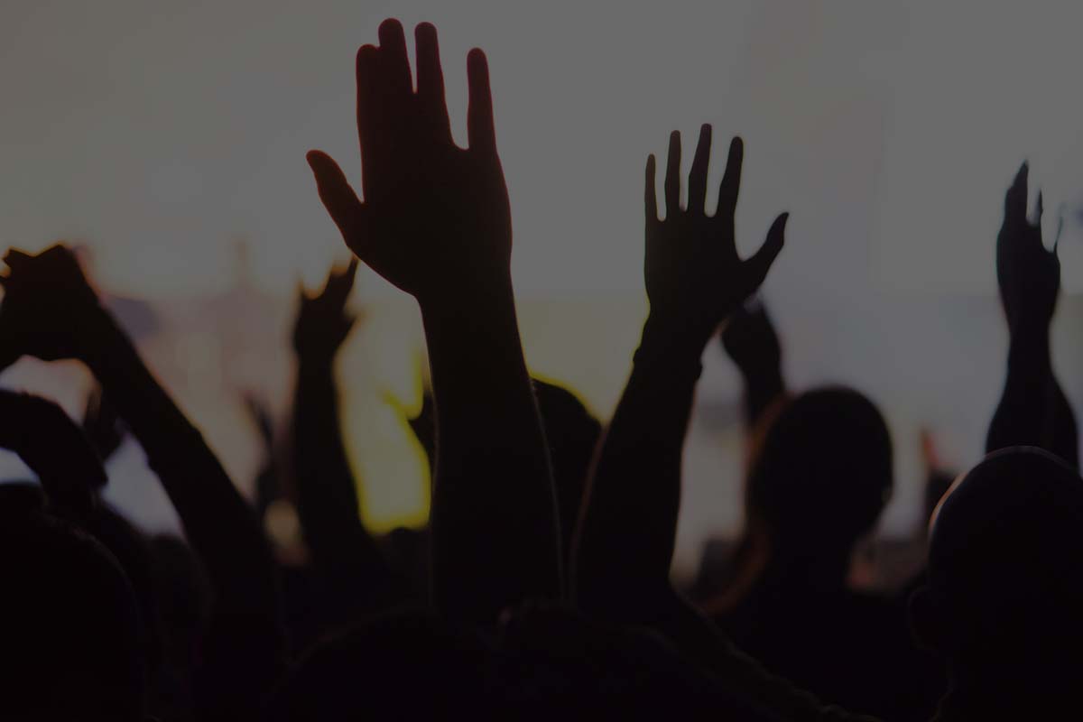 A crowd level view of hands raised from the spectating crowd interspersed by colorful spotlights and a smokey atmosphere